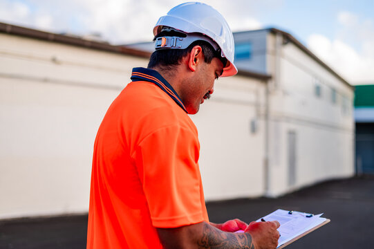 A construction worker in bright orange checks notes while standing outdoors at a building site