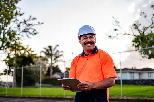 Man in safety gear smiles while reviewing notes outdoors at a construction site