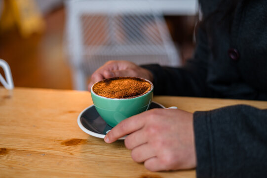 Female hand holding a cup filled with coffee on a wooden table in a cafe