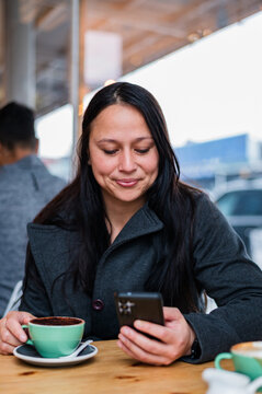 Woman with long hair looks at her phone while seated in a cafe table