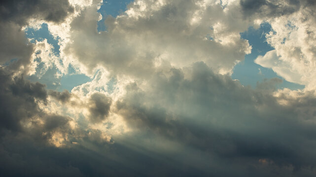 Sun rays streaming through clouds in clear blue sky