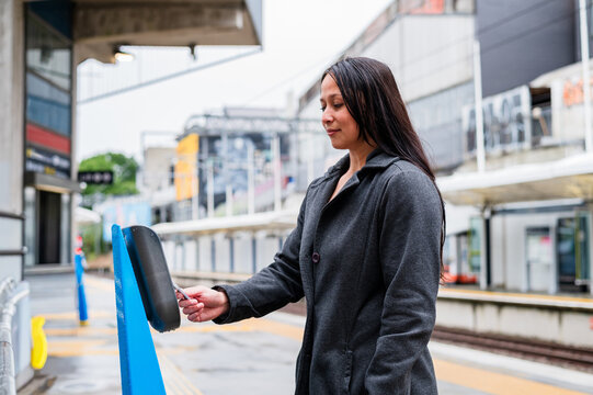 Woman taps her card on the ticket machine at a train station in New Zealand during a rainy day