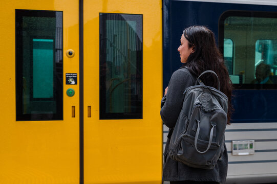 Woman stands near train doors at a New Zealand station in light rain with a backpack