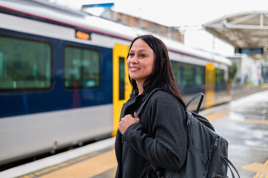 A woman stands at a train station with a backpack while it rains