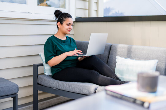 Indian woman sits on a couch and working on her laptop in a New Zealand residence
