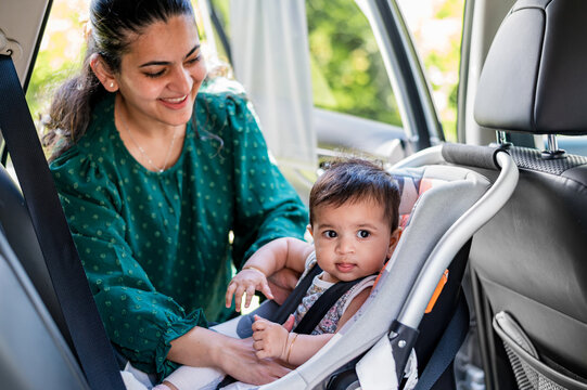 Mother buckling baby into rear-facing car seat inside a vehicle during day time in a parked position
