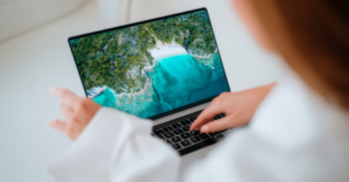 woman in her thirties, dressed as travel agent showing to couple laptop screen with beautiful beach on it and world map behind them, sitting at desk facing camera