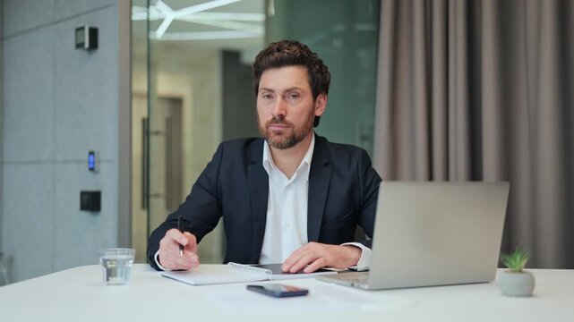 Professional working diligently, taking notes at a contemporary office desk. Demonstrates concentration and dedication in business environment, representing success and productivity.