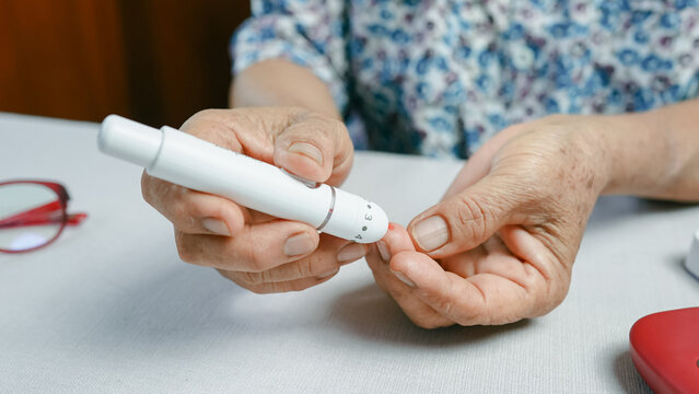 Close up of senior woman using lancet device for finger prick blood test, showing diabetes monitoring and glucose control. Elderly healthcare and chronic disease management concept.