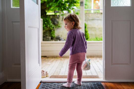 Toddler girl walking out the door carrying a bucket of colourful chalk