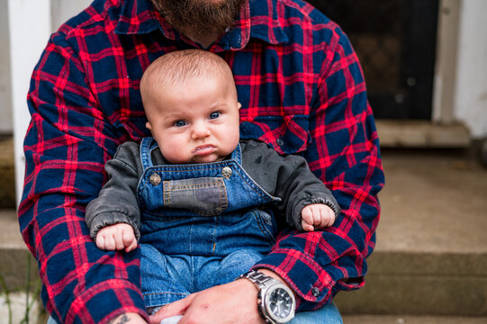 Baby boy seated on fathers lap sitting on concrete steps