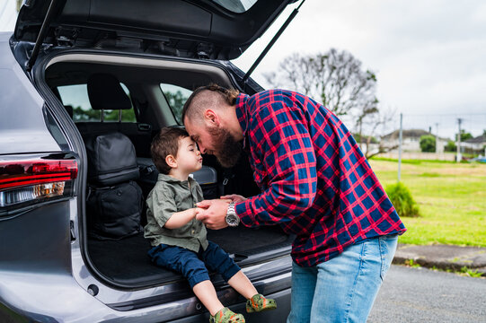 Father leaning forward touching foreheads with son seated on car boot