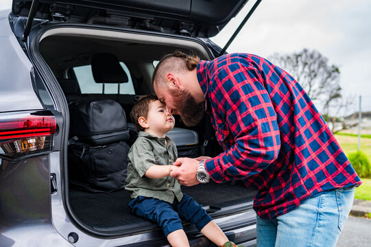 Father leaning forward touching foreheads with son seated on car boot