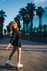 Naklejka premium Confident roller skater glides through urban path at dusk, wearing headphones and black outfit, arms mid-motion in elegant rhythmic movement combining music, sport, and style.
