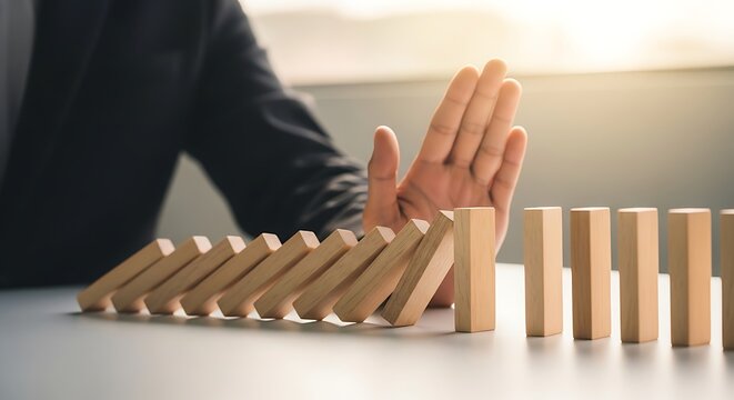 Business person's hand stopping a line of falling dominoes, illustrating risk mitigation, crisis intervention, and proactive strategy
