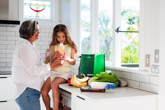 A child sitting in the kitchen counter, looking into the bottle label with grandmother