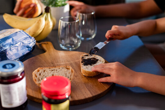 Child hand spreads marmite on a slice of bread on a round wooden board