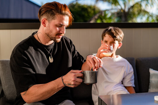Father sharing a meal with tween son while seated on the couch in the balcony