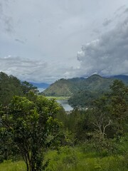 Fototapeta premium Scenic view of a mountain valley with a lake surrounded by green forest under a dramatic cloudy sky. Represents nature, travel, and outdoor landscape beauty.