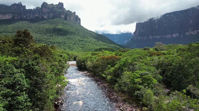 Aerial drone view of a tropical river flowing through dense rainforest surrounded by the dramatic tepui mountains in Canaima National Park, Venezuela