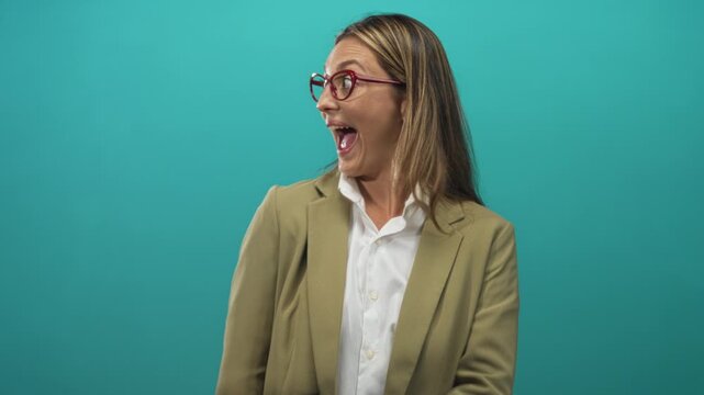 Woman with open mouth and red glasses turning head, wearing khaki blazer and white shirt in studio with turquoise backdrop; surprise energy.