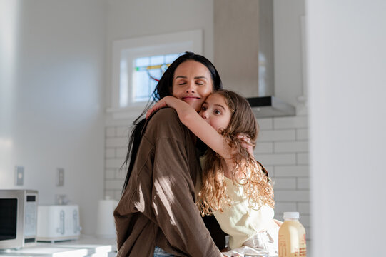 Young maori girl seated on kitchen counter hugging mum