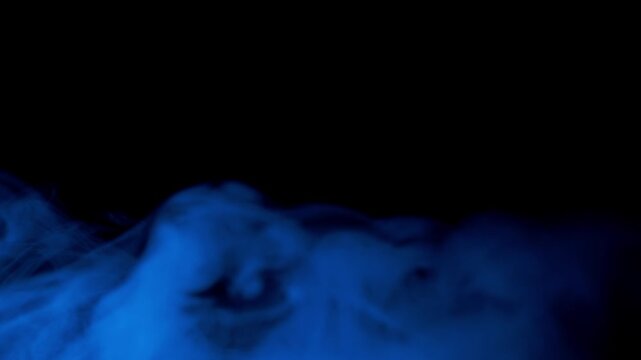 Thick clouds of teal and blue smoke drift slowly upwards from the bottom against a dark backdrop. Concept of mystery, creativity, chemical reactions, and atmospheric effects.