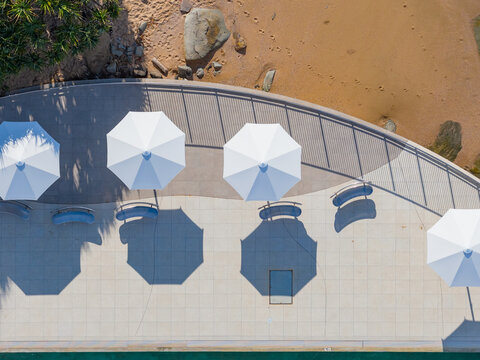 Aerial view of white poolside umbrellas casting shadow patterns on a paved deck