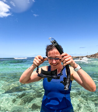 Woman snorkelling in clear blue green water adjusting snorkel and mask with sun shining