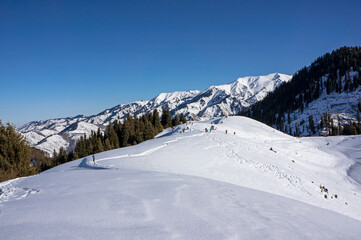 Obraz premium Crowded winter mountain trail at Kok Zhailau plateau with hikers and scenic view of Tian Shan peaks