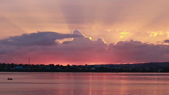 a fisherman who is rowing his traditional boat (sampan) slowly. The light of the setting sun reflects beautifully on the slightly rippling surface of the water.