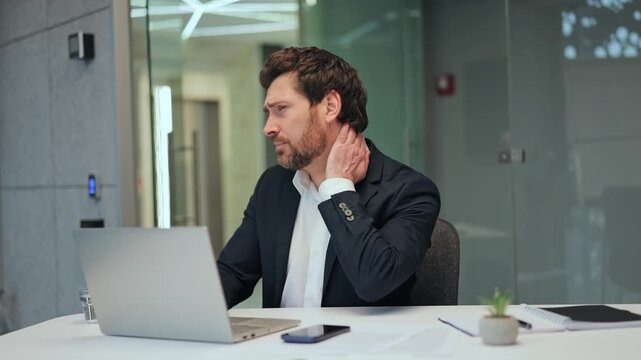 Focused professional experiences neck discomfort while working on a laptop. Illustrates pain, fatigue, and stress from prolonged computer use in a modern office environment.