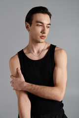 Fototapeta premium Young man showcases modern fashion in black tank top against grey background
