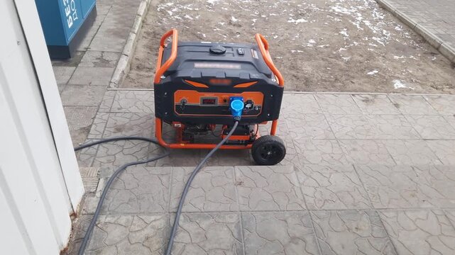 Portable gasoline generator provides backup electricity outdoors on a paved area. A thick power cord with a blue industrial plug is connected to the working unit.