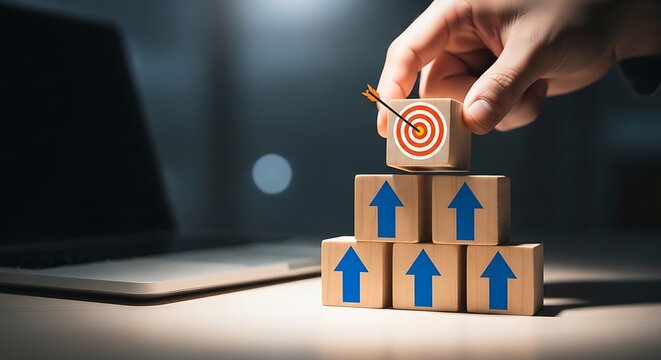 A hand placing a target block atop a stack of upward-pointing blocks on a desk.