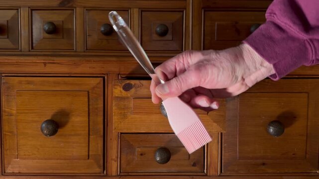 A senior man&rsquo;s hand opening and closing a drawer in an old pine kitchen dresser, to remove a pink silicone pastry brush.