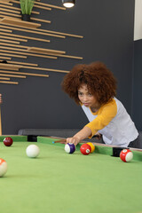 Teen friends playing on green pool table in game room, wearing raglan, aiming cue, copy space