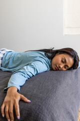 Obraz premium Asian woman lying face down on dark gray duvet with pillow in bedroom, wearing blue top