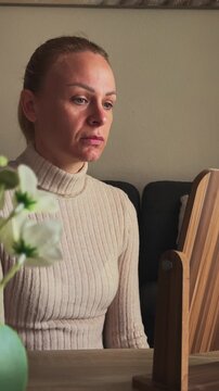 Pensive middle-aged woman sitting alone at home, looking at her reflection with a sad expression, touching her face and worrying about wrinkles, skin aging, and beauty