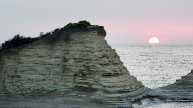 Dramatic aerial shot panning across the unique layered rock formations and sea stacks of Canal d'Amour at sunset. Sidari, Corfu, Greece