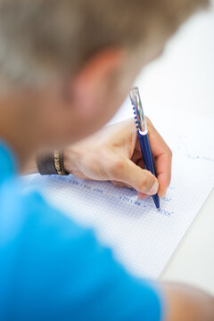 Sch&uuml;ler schreibt mit Kugelschreiber mathematische Berechnungen und Fl&auml;chenformeln in ein kariertes Heft, Fokus auf Hand und Schulaufgaben