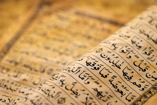 Pages of Al Quran Muslim old holy book on table in mosque. Details of arabic calligraphy in islamic book. Concept of Islam religion and praying in arabic countries