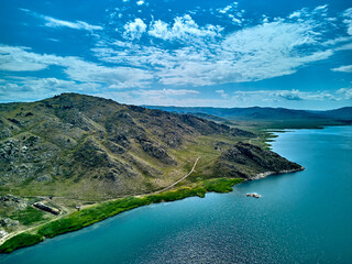 Obraz premium Aerial view of a remote sandy beach and rugged coastline with mountains and island under a moody sky, on the Bukhtarma Reservoir, on the Irtysh River, in Kazakhstan (Qazaqstan)
