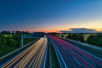 Obraz premium German Autobahn at Sunset with Long Exposure Light Trails and Gantry Sign