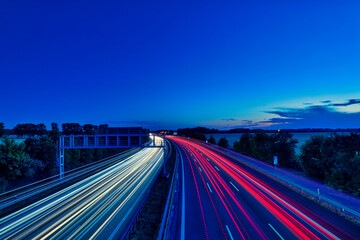 Obraz premium German Autobahn at Sunset with Long Exposure Light Trails and Gantry Sign - real photography - authentic - no ai