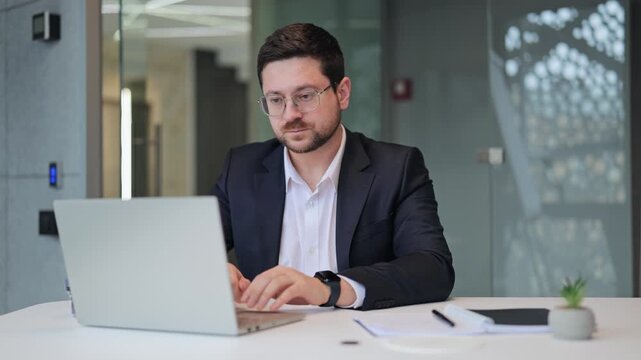 A dedicated business professional begins work, opening a laptop and typing diligently at a modern office desk. Displays commitment and focused effort toward achieving professional goals.