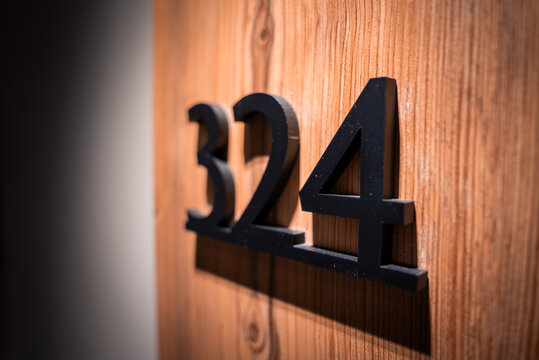Room number 324 appears in matte black three dimensional numerals on a wooden door with grain. Warm directional light casts crisp shadows, suggesting San Domenico.