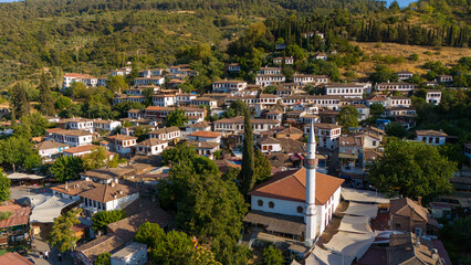 Obraz premium Aerial view of a traditional Turkish village with white houses, red roofs and a mosque surrounded by green hills. Scenic rural landscape and authentic architecture in Turkey.