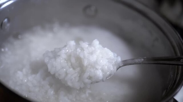 A close-up of a spoon lifting cooked rice from a pot, showing the thick, creamy consistency of rice porridge. Ideal for food blogs and cooking shows.