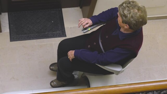 Senior female riding electric stairlift chair up residential stairs in modern house for easy access